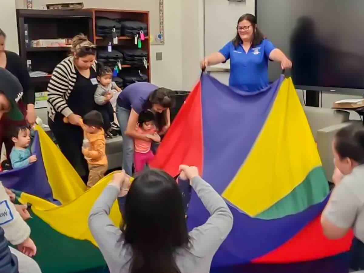 Parents Place staff lead a classroom full of kids through a parachute activity.