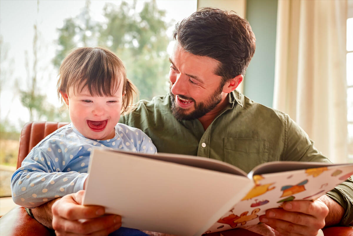 A father joyously reads a storybook with his daughter with Down syndrome